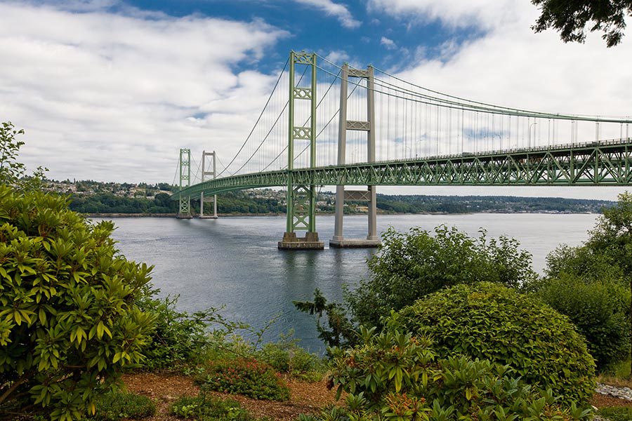 About Our Agency - Tacoma Narrows Bridge on a Sunny Day With Greenery in the Foreground
