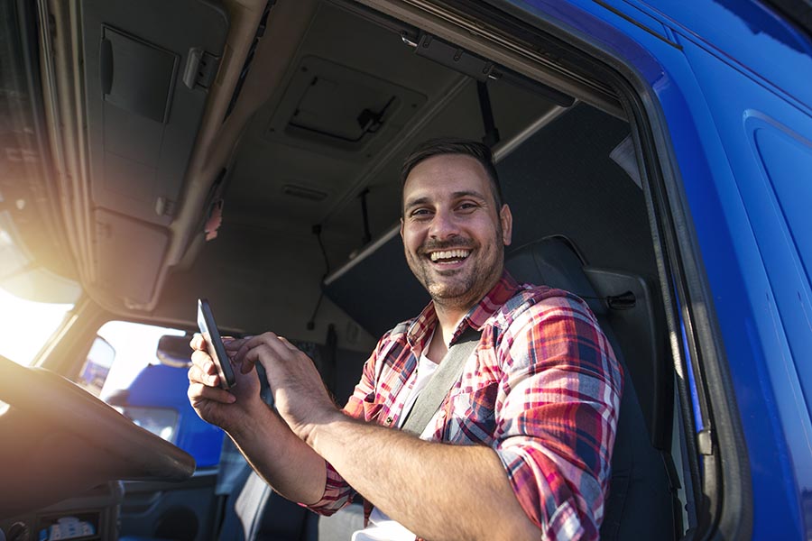 Business Insurance - Truck Driver Smiles From Inside the Cab of His Blue Semi, Wearing Red Flannel