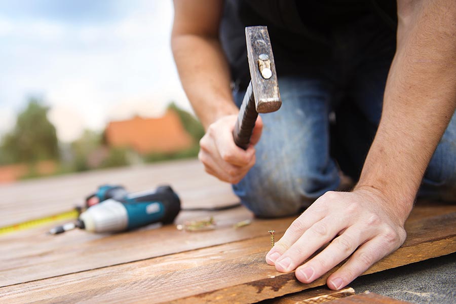 Specialized Business Insurance - Man Hammers a Nail Into Decking With a Measuring Tape and Drill Nearby
